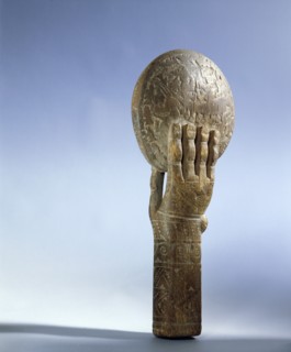 Wooden hand holds a disc on which are carved mythological scenes