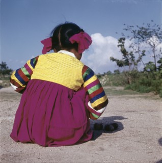 A young Korean girl in brightly coloured national dress, crouching on the ground as she plays a game