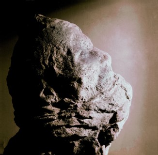 Cast of a man's head with his mouth partly covered with lava
