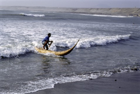 Modern day Moche fisherman guiding a tortora reed boat (caballito) on beach on Peru's northern coast