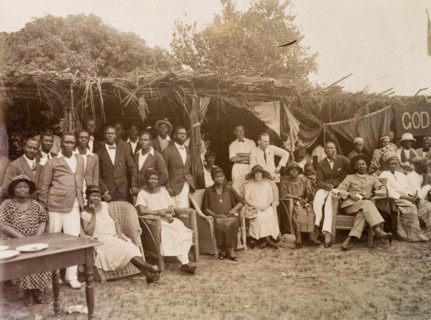 Group standing and seated under palm frond awnings