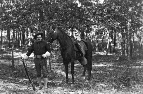 A member of the cavalry poses standing in front of his horse