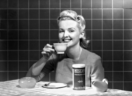 United States:  c. 1960.
A single woman at a kitchen table enjoys a cup of Nescafe.