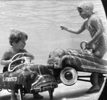 United States:  c. 1958.
Two children move their playground toys into the pool, where accidents