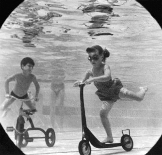 United States:  c. 1958.
A group of children move their playground toys into the pool.