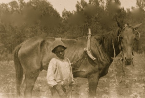 African American boy standing with horse attached to plow 1899