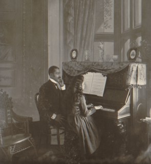 African American Man in suit gives piano lessons to a young white girl 1900