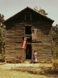 African American woman standing by building with Georgia state and United States flags. 1941