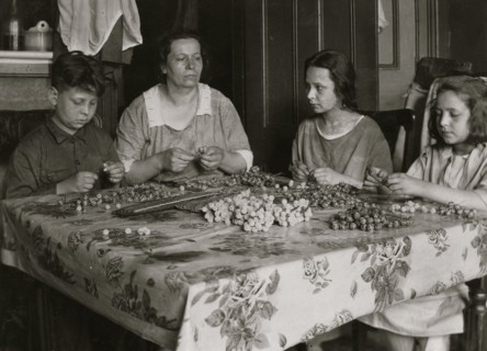 Cottage Industry shows family stringing material in piecework done at home. 1924