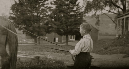 Eight-year old Jack carrying cans of milk on stone boat. This involves some heavy lifting 1915
