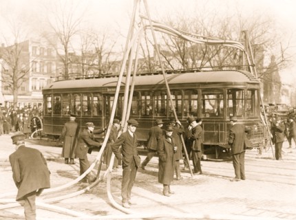 Firemen with hoses over streetcar 1914