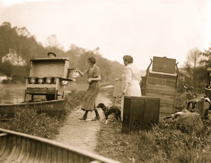 Folks carry a range out their home to escape rising water in a flood; a women holds their pet dog on a  leash 1924