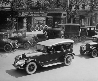Ford cars in procession drives past a bargain tire retail store in DC