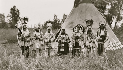 Group of Siksika (Blackfeet) men and one woman singing in front of tipi 1913
