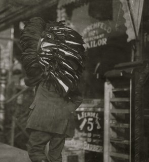 Man loaded down with heavy bundle of vests that he had been carrying for many blocks, stopping to rest, occasionally, when he would drop the bundle down onto whatever boxes or railings were available,...