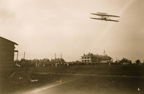 Orville Wright flying in his airplane, crowd on field 1908