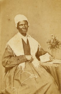 Sojourner Truth, three-quarter length portrait, seated at table with knitting and book 1864