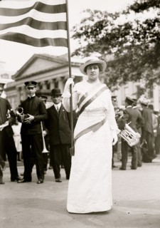 Suffragette holds flag at the head of a waiting male band 1913