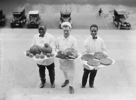 Three Chefs stand on bottom of a line of steps and hold up Thanksgiving platters of Pies, apples and a Turkey 1922