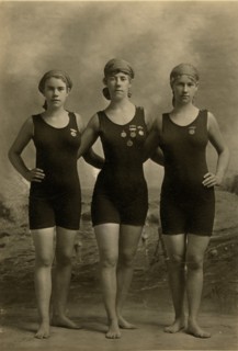 Three young women posing in swimsuits and wearing their swimming competition medals 1920