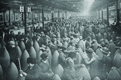 Throngs of women interspersed amongst large artillery shells on a factory floor. 1917