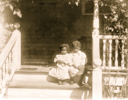 Two African American children sitting on steps to porch 1899