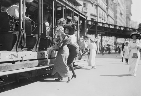 Woman lifts child off of an open sided Trolley Car on New York's Broadway