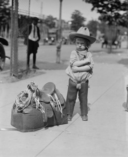 Young Cowboy, "Fog Horn Clancey" stand beside saddle bag and lasso 1923