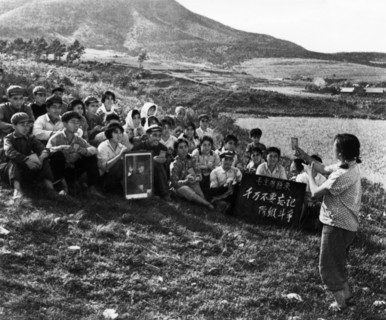 During a work break, a young woman is leading the commune workers in singing a song praising chairman mao, cultural revolution, tachai, shansi province, china, 1968.