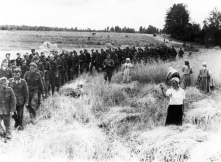 A soviet woman harvesting in a field torn by shells only a short time ago, shakes her fist at a line on nazi pows marching eastward under guard, feb,14, 1944.