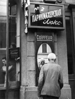 A peasant who came to moscow from the provinces, stops to look at himself in the street mirror of a barber shop,  his hair has been 'bobbed' as millions of peasants of former russia customarily trimme...
