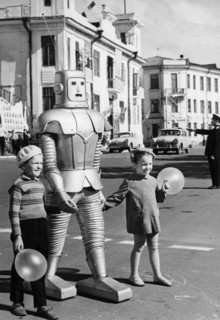 A robot belonging to local circus performer oleg sokol helping two children with balloons cross the street in arkhangelsk, ussr, 1967, the robot is part of the technical illusion attraction 'wonders w...