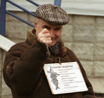Moscow, russia, november 25 2002: ukrainian gastarbeiter (guest worker) with an attached poster enumerating kinds of flat repair work keeps his post in one of illegal labour markets that still exist i...