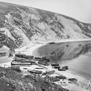 Fishing village on Lulworth Cove with boats on the shore and cliffs along the coast