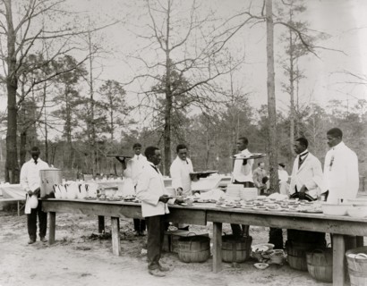 African American men preparing to serve a meal in an outdoor setting among trees