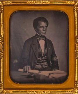 Beverly Page Yates, half-length portrait, facing slightly right, seated at table, holding rolled piece of paper