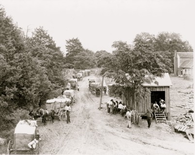 African Americans around small building and wagons loaded with cotton
