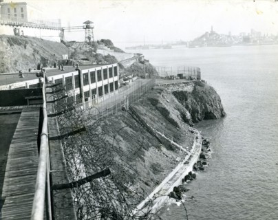 Alcatraz Prison, San Francisco, CA, circa 1940 - A view of the island taken from the industrial area with a guard tower, main cellhouse and San Francisco skyline in the background.