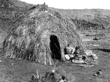 Edward S. Curits Native American Indians - Rounded structure made out of grass, with baskets in front circa 1903.