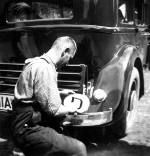 Life in Germany circa 1930s - German man affixing a country sticker to his car bumper.