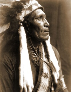 Edward S. Curtis Native American Indians - Raven Blanket, wearing several necklaces and warbonnet with ermine streamers circa 1910.
