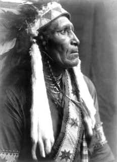 Edward S. Curtis Native American Indians - Raven Blanket, wearing several necklaces and warbonnet with ermine streamers circa 1910.