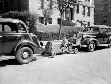 A boy occupies a parking spot in his home made go-kart circa 1937.