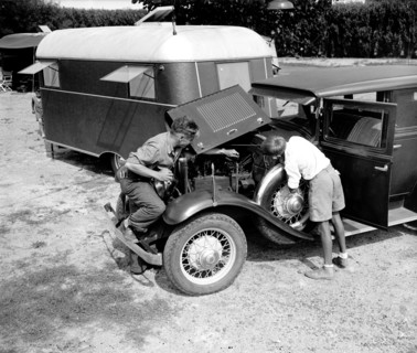 Man and his son looking under the engine and working on their car at a trailer camp circa 1937.