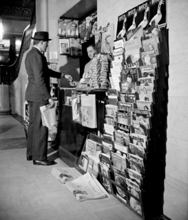 Man paying worker for a newspaper at indoor newspaper stand (news stand) circa 1940.