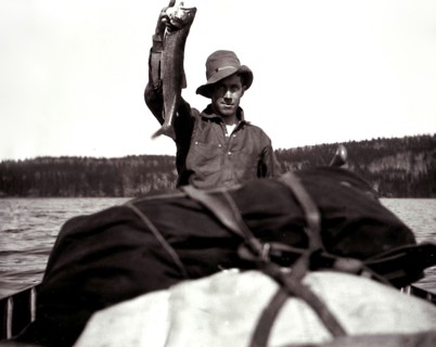 A man in a canoe, holding up a fish circa 1909.