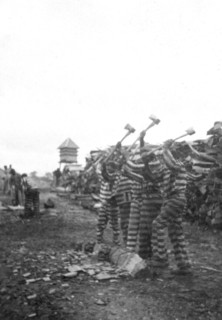 African American convicts working with axes, watchtower in background, Reed Camp, South Carolina circa 1934.