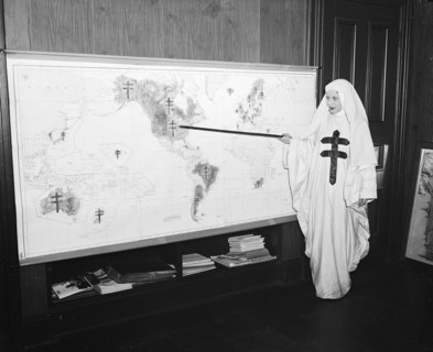 Miss Mildred Showalter of Washington, dressed as the Spirit of the Double-barred cross of the anti- tuberculosis movement throughout the world, points to various battlefronts throughout the world wher...
