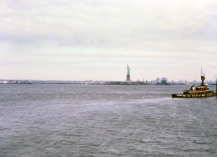 (R) New York 1975 - Tugboat in water in front of Statue of Liberty in New York City in mid-1970s.
