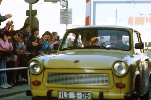 West German children applaud as an East German couple drive through Checkpoint Charlie and take advantage of relaxed travel restrictions to visit West Germany..
